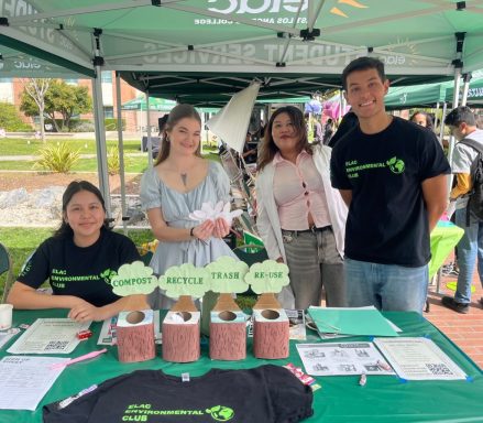 Group of four people at an outdoor informational booth with green canopies and brochures.