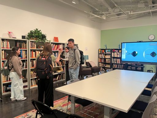 People engaging in conversation in a room filled with bookshelves and a large screen.