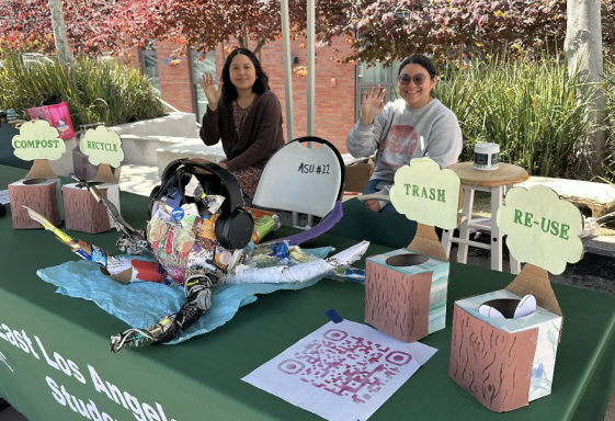 Two women smile behind a table with colorful recycling and reuse items on display.